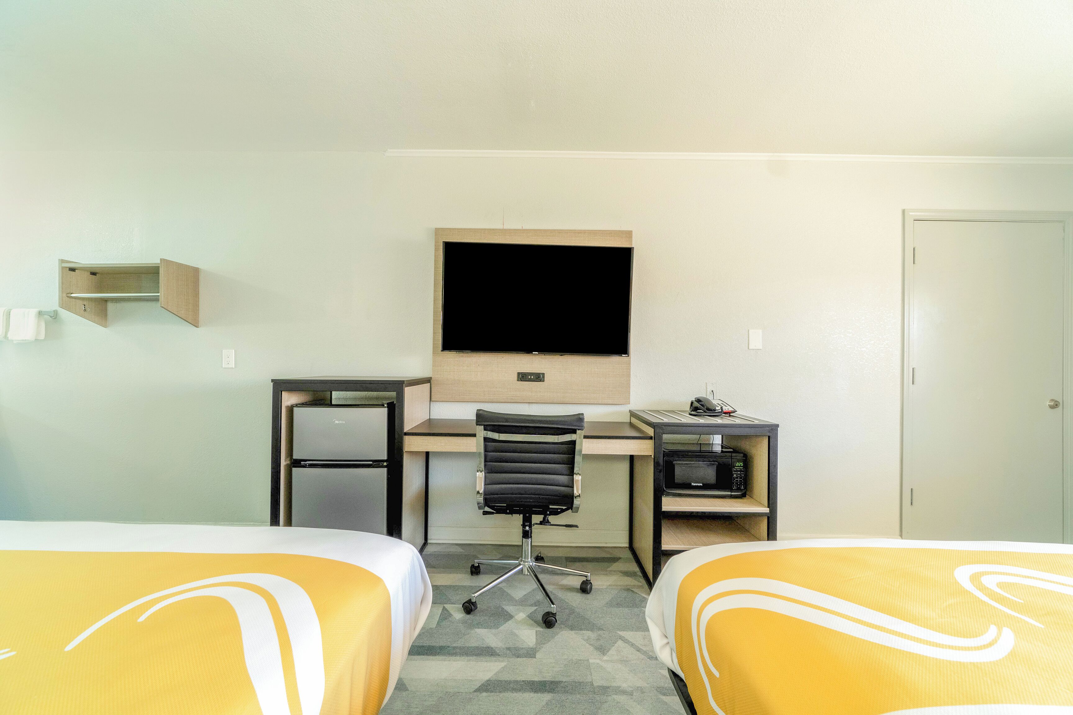 A hotel room with two beds, a desk with a computer, a TV, and a microwave.