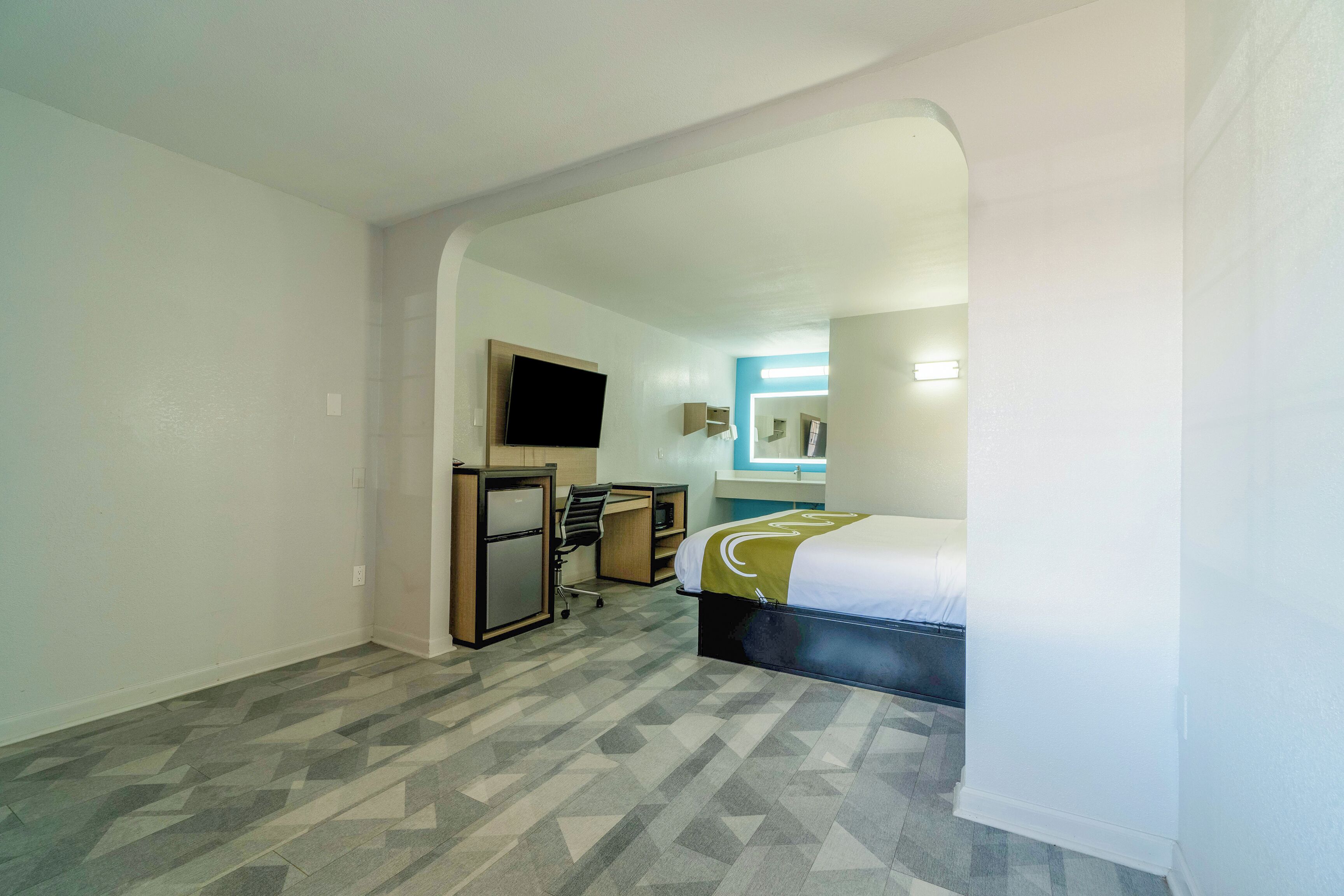 Habitación de hotel con cama, escritorio, silla y televisor.