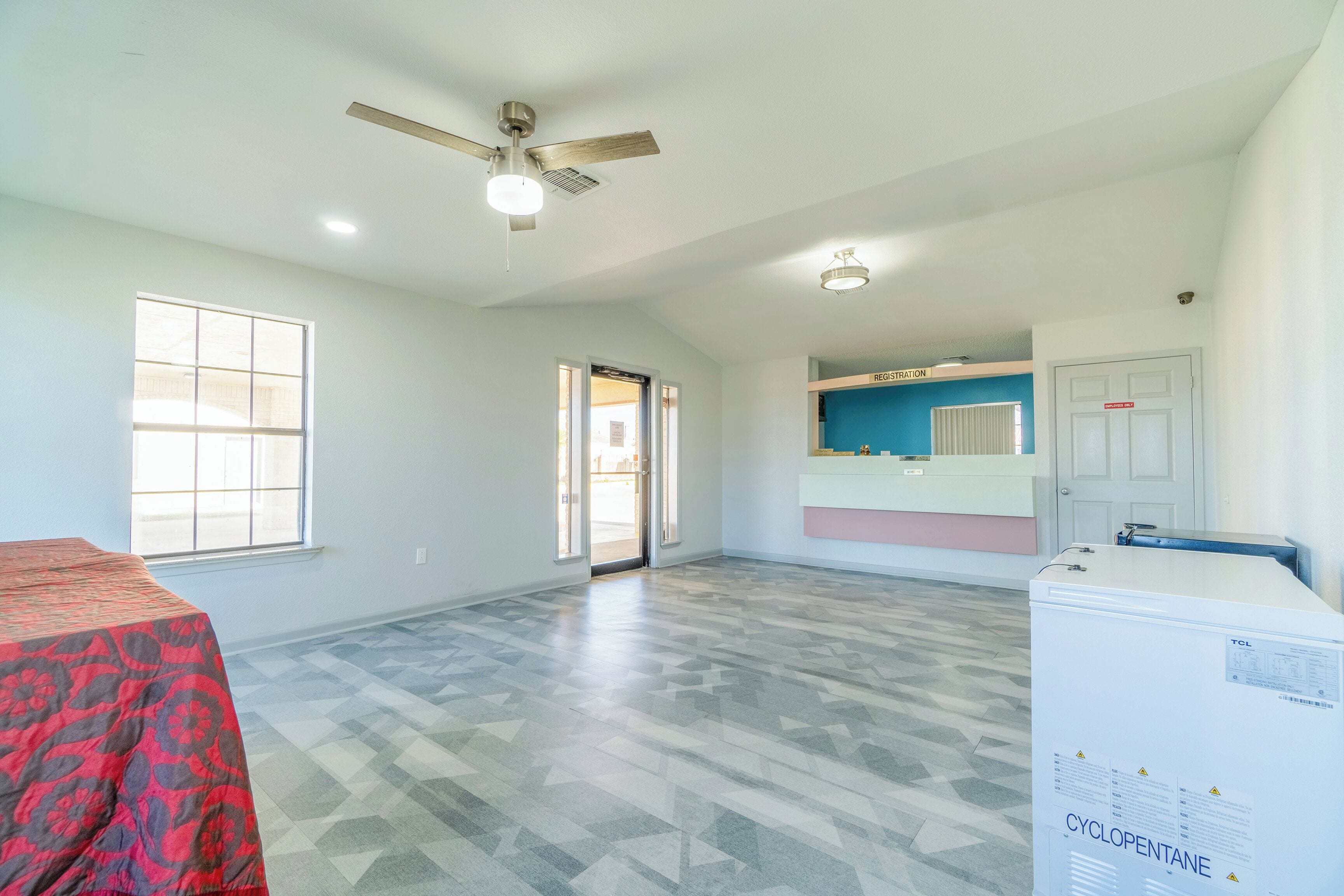 A spacious room with a patterned floor, a ceiling fan, and a refrigerator with a warning label.