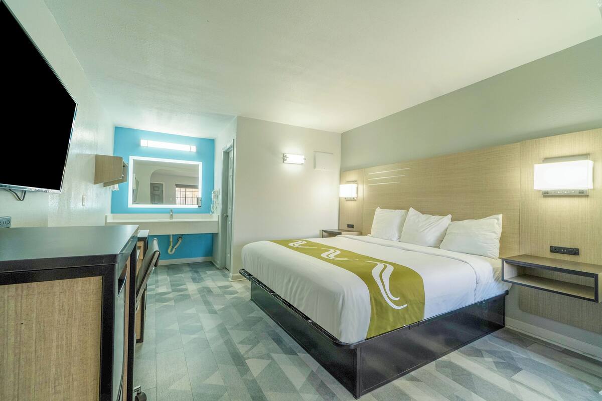 Una habitació d'hotel amb llit, una taula de nit i un televisor penjat a la paret.