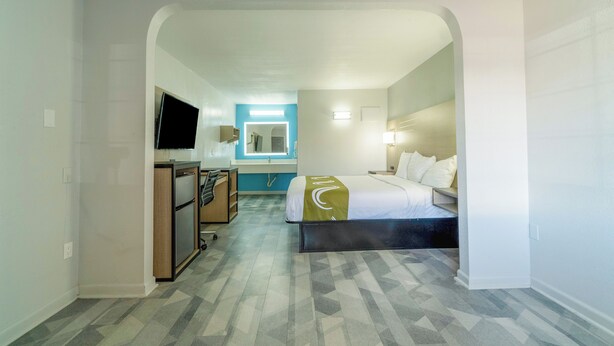 A hotel room with a bed, a desk, a television, and a bathroom visible through an archway. - Pleasanton Executive Inn By OYO (Pleasanton)