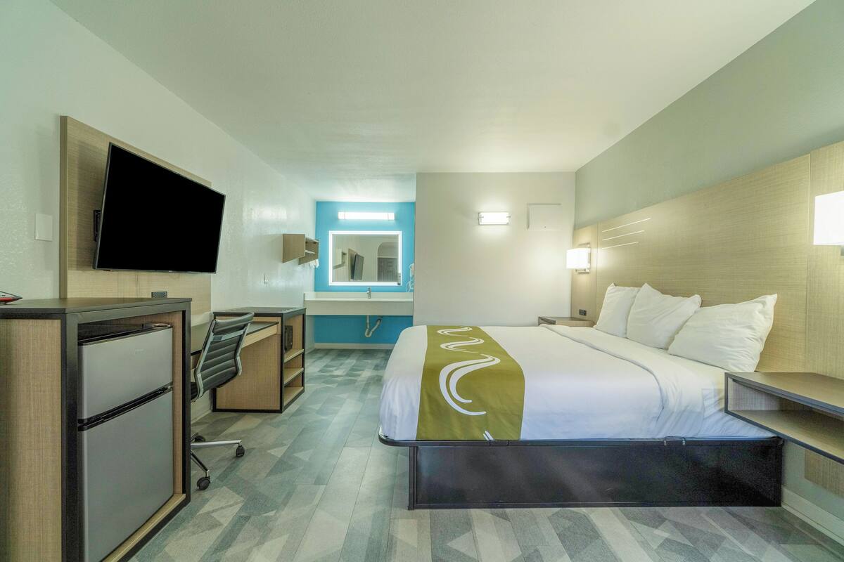 Habitació d'hotel amb llit, escriptori, cadira, televisió i bany amb mirall i rentapous.