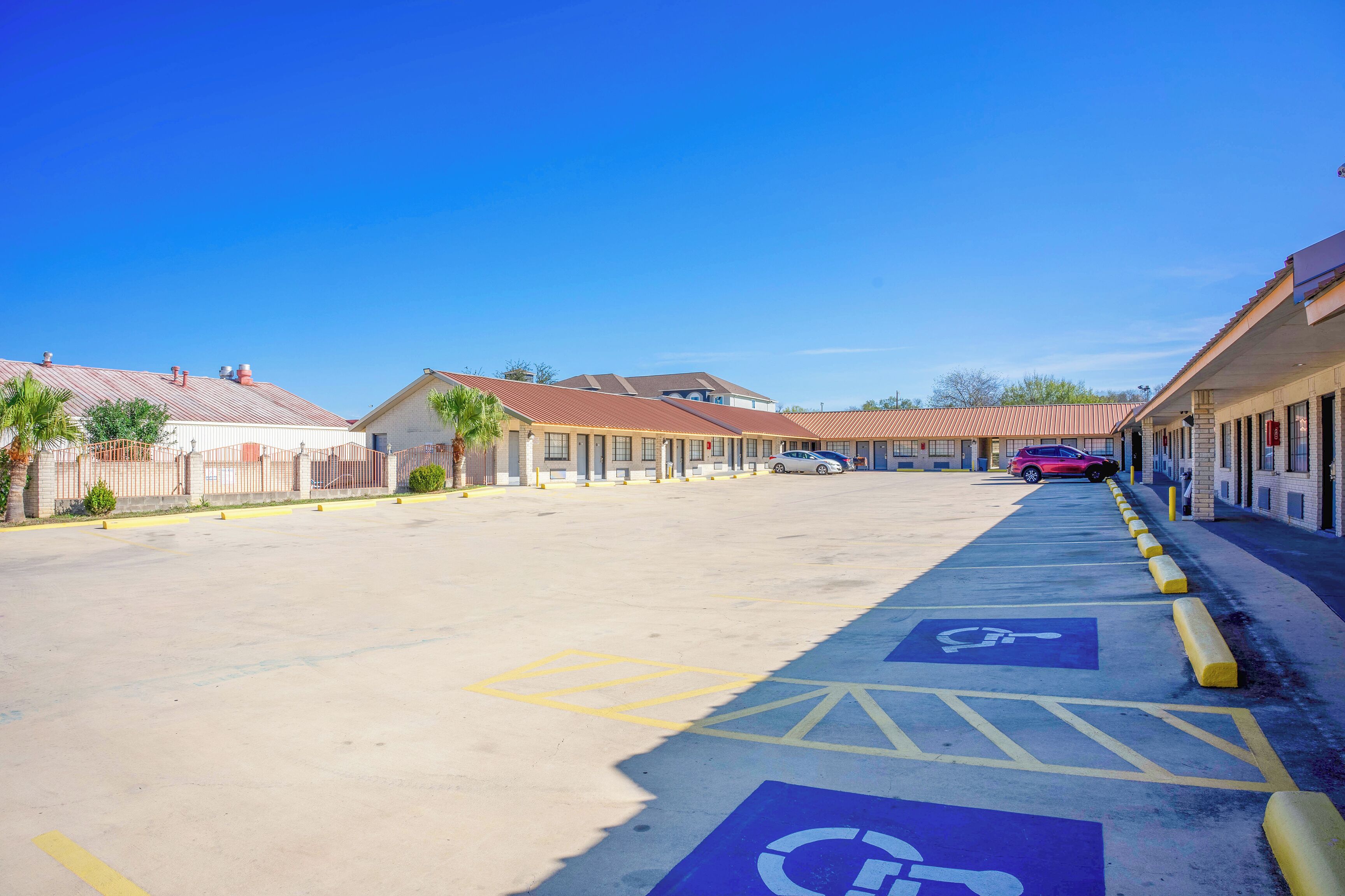 A parking lot with handicapped parking spaces, a row of buildings with a red roof, and a clear blue sky.