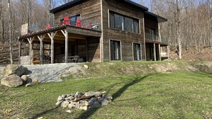 Ein modernes Blockhaus mit überdachter Veranda, zahlreichen Fenstern und einer Feuerstelle aus Stein.