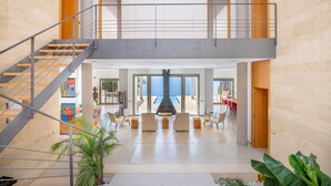 A spacious interior with a central seating area, a staircase, and a view of the sea. - Villa Beachfront - Herce Property by Priority (Llucmajor)