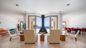 A spacious living area with a fireplace, two sofas, a coffee table, and a view of the sea through large glass doors. - Villa Beachfront - Herce Property by Priority (Llucmajor)