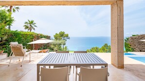 A covered outdoor seating area with a table and chairs, overlooking a pool and the sea. - Villa Beachfront - Herce Property by Priority (Llucmajor)