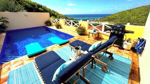 Un área de piscina en la azotea con sillones de descanso, una parrilla y vista al océano.
