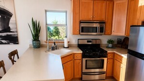 A modern kitchen with wooden cabinets, stainless steel appliances, a large window, and a dining area.