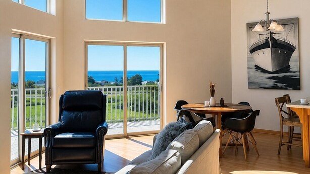 A spacious living room with large windows, a ceiling fan, a dining area, and a view of the ocean.
