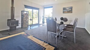 A modern living room with a fireplace, a dining table with chairs, a large window, and a painting on the wall. - A Yingina Getaway, Home of Brown Trout (Miena)
