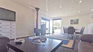 A modern living room with a fireplace, a flat-screen TV, a dining area with chairs, and a large window. - A Yingina Getaway, Home of Brown Trout (Miena)