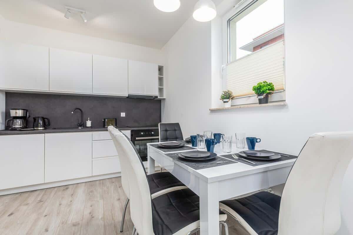 Une cuisine moderne avec des meubles blancs, un plan de travail noir et un coin repas comprenant une table blanche et des chaises noires.