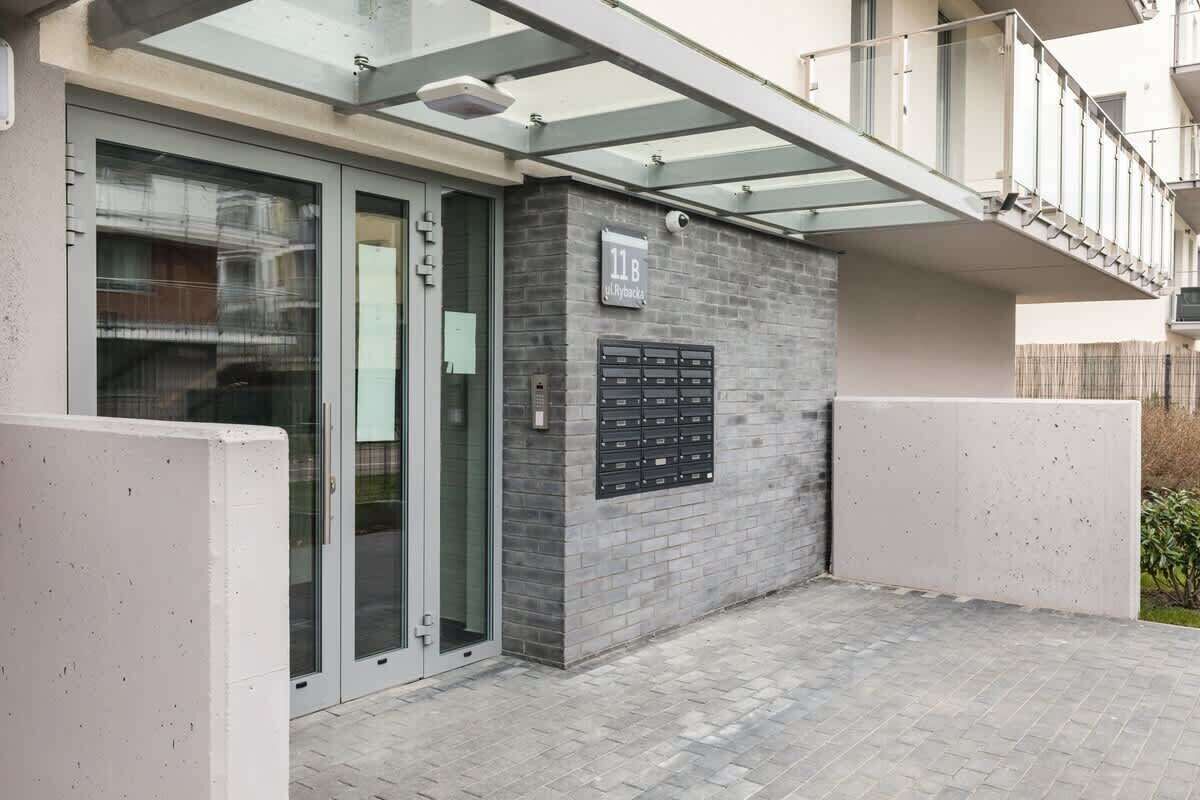 Una entrada de edificio moderna con puerta de cristal, buzón y un pequeño espacio exterior con suelo de baldosas.