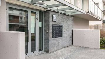 A modern building entrance with a glass door, a mailbox, and a small outdoor area with a tiled floor.