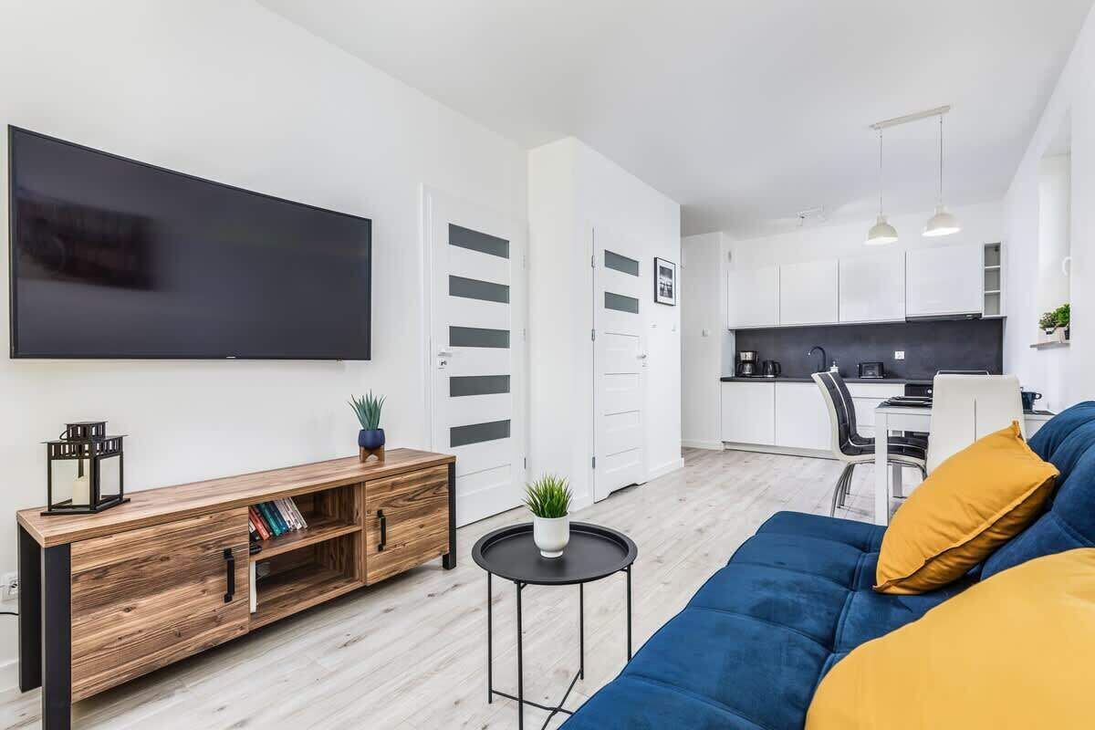 Un salon moderne avec un téléviseur à écran plat, un canapé bleu, une console en bois et une petite table ronde agrémentée d’une plante.