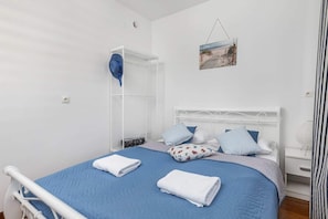 A bedroom with a bed, a white metal headboard, a blue bedspread, and a white bedside table with a lamp.