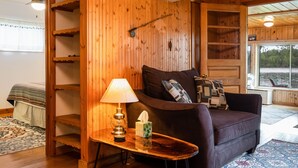 A cozy cabin interior with a wooden wall, a sofa, a lamp, and a window with a view. - Clam Lake Waterfront Cottage (Bellaire)