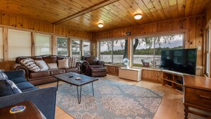 A wooden cabin interior with a sofa, armchair, and TV. - Clam Lake Waterfront Cottage (Bellaire)