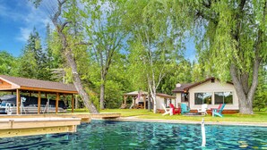 A swimming pool with lily pads, surrounded by trees and a small house with outdoor seating. - Clam Lake Waterfront Cottage (Bellaire)