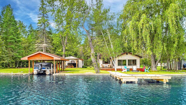 A lakeside property with a dock, a covered area with a boat, and a house with outdoor seating. - Clam Lake Waterfront Cottage (Bellaire)