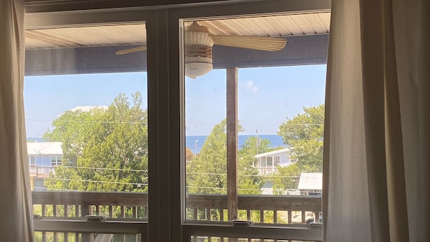 Blick von einer überdachten Veranda mit Holzbalkon, einer Pendelleuchte und blauem Himmel.