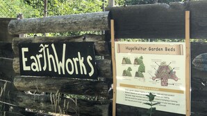 A wooden sign with the text "EarthWorks" and a poster about Hugelkultur Garden Beds. - Glamping #4, Nature Immersion, River access, Butterfly Pavilion (Cave Junction)