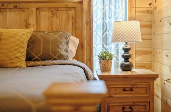A wooden cabin room with a bed, a nightstand with a lamp, and a potted plant.