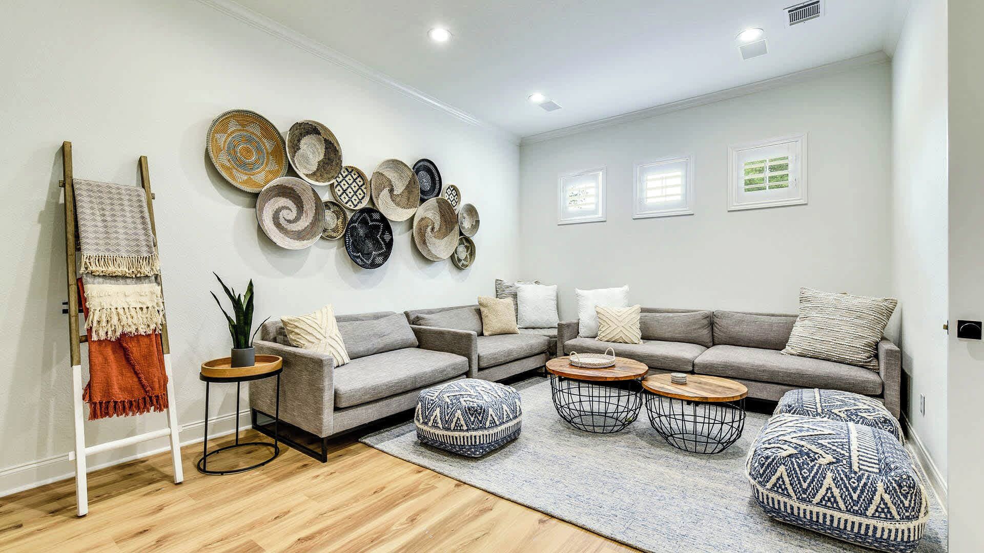A modern living room with a grey sectional sofa, round coffee tables, and a variety of woven baskets on the wall.