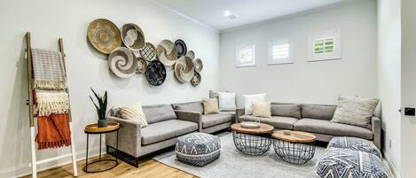 A modern living room with a grey sectional sofa, round coffee tables, and a variety of woven baskets on the wall.