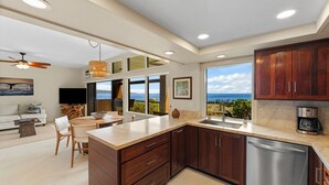 A modern kitchen with a view of the ocean, wooden cabinets, and a built-in dishwasher. - Ridge 1712- Ocean View w/Platinum Interiors! (Lahaina)