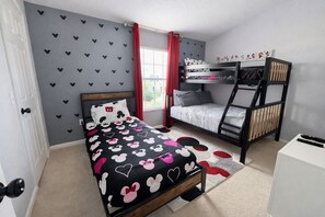 A bedroom with a bunk bed, a single bed with a Mickey Mouse themed bedspread, a window with red curtains, and a wall with Mickey Mouse cutouts.