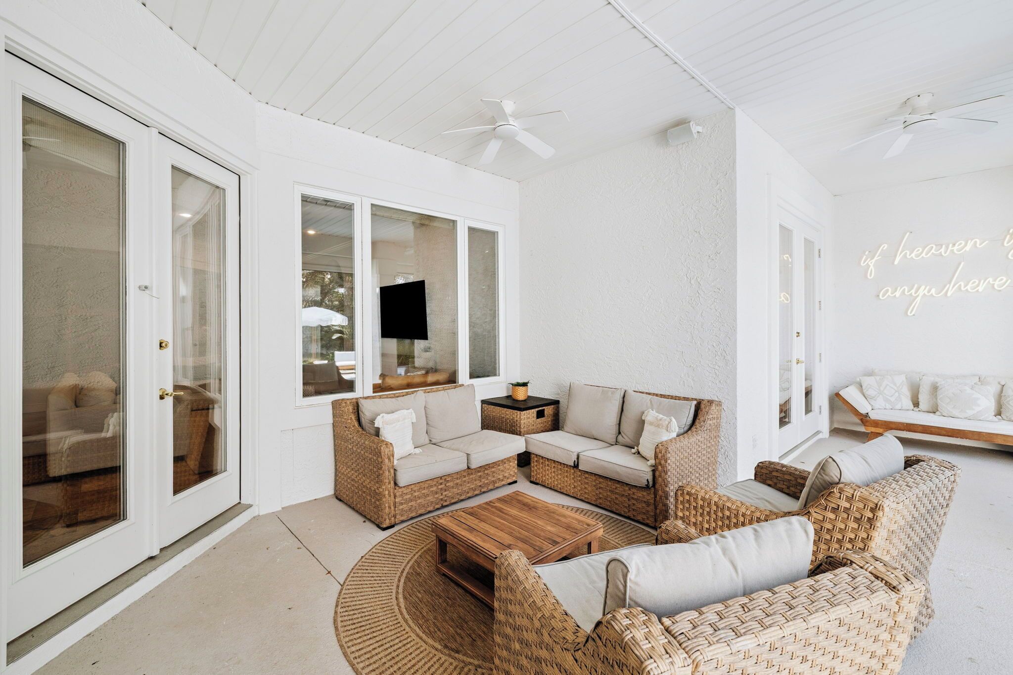 A white interior with wicker furniture, ceiling fans, and a wall with a neon sign.