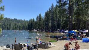 A lakeside beach with kayaks, tents, and people enjoying the water. - Preferred Parking Pass to Dodge Ridge (Cold Springs)