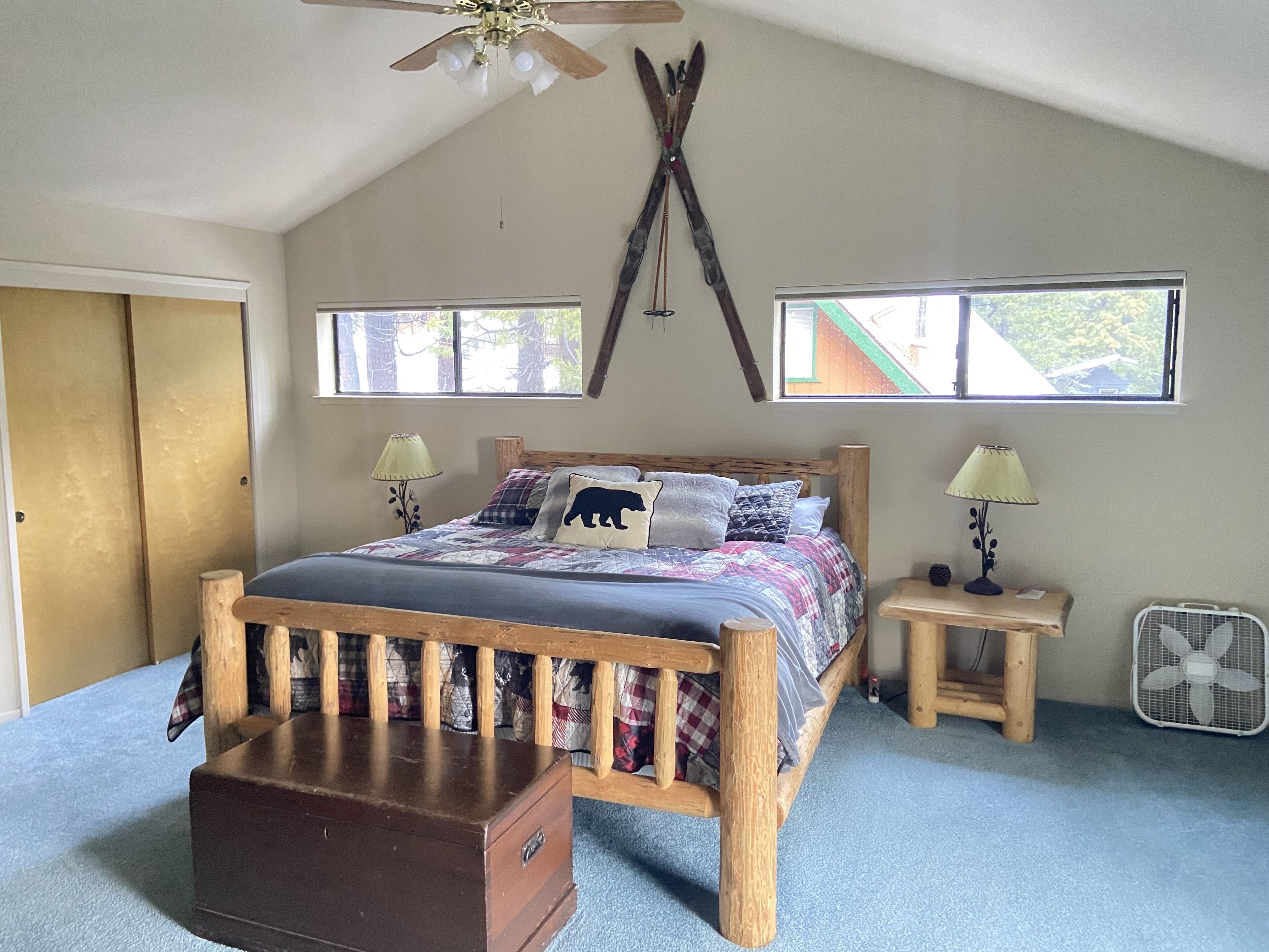 A bedroom with a wooden bed, two bedside tables with lamps, a ceiling fan, and a large window.