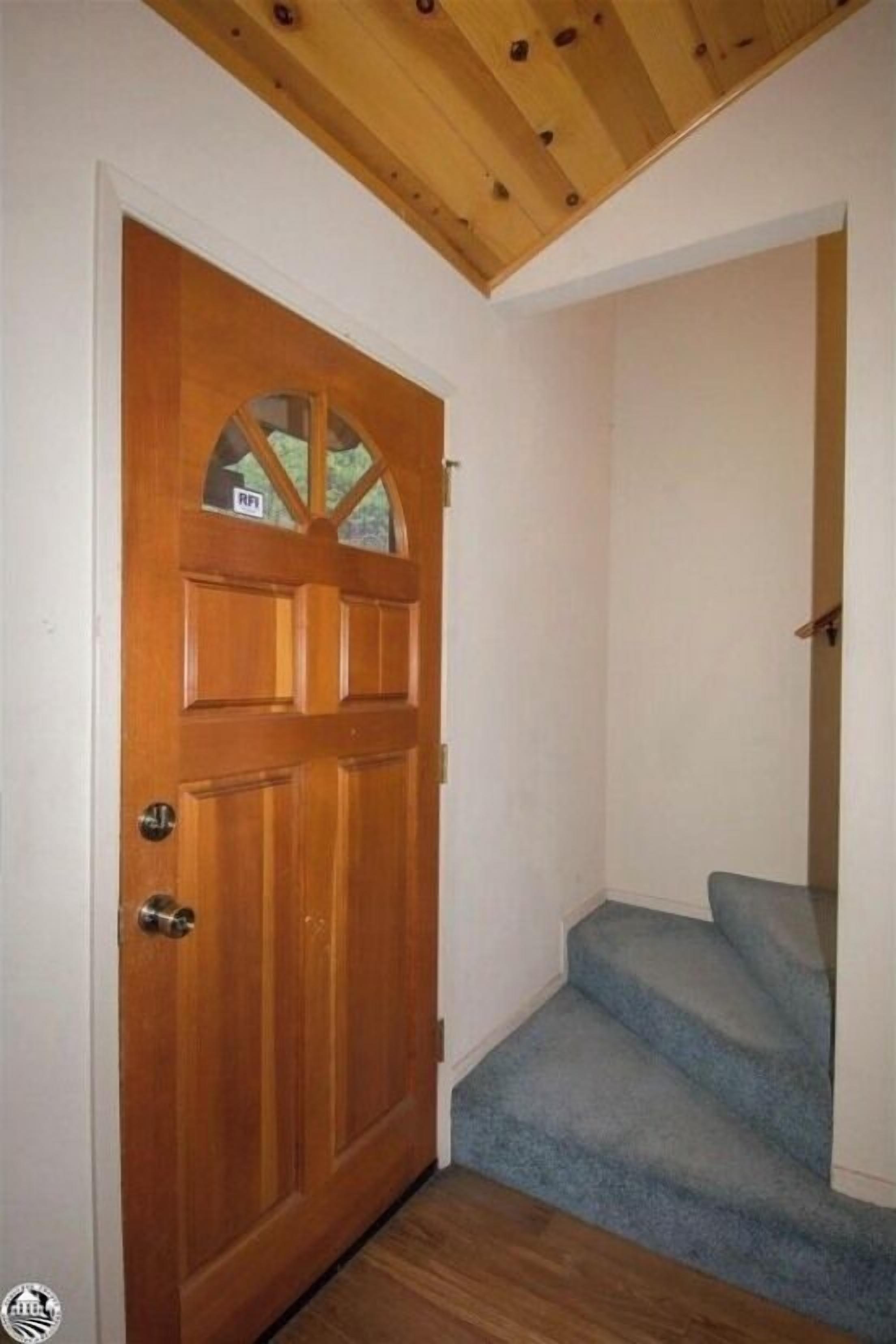 A wooden door with a glass panel and a small window, leading to a staircase with blue carpet.