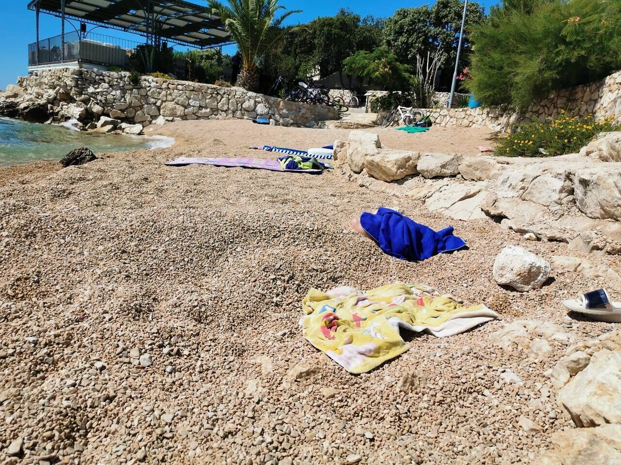 A pebble beach with a stone wall, a covered area, and bicycles.