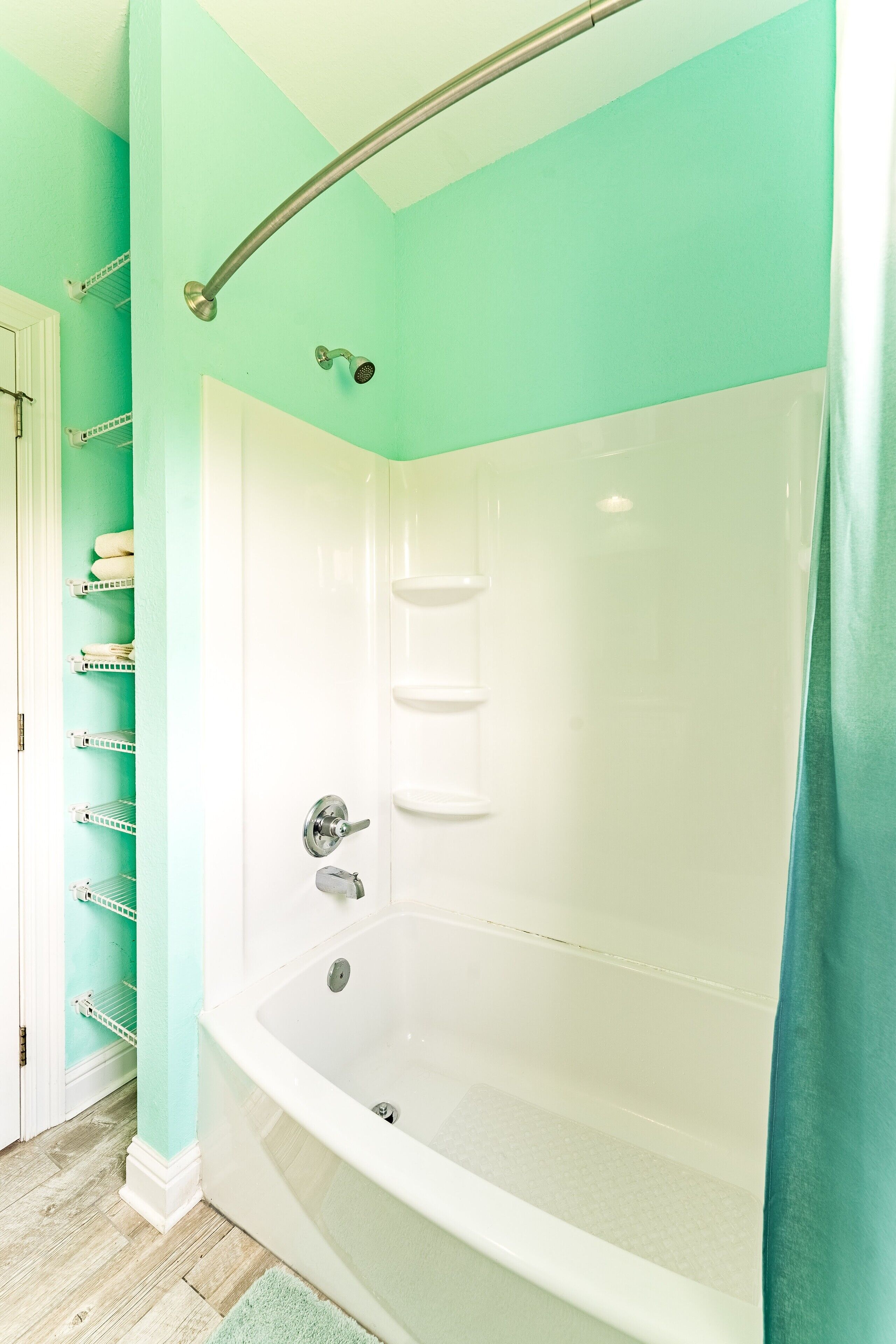 A bathroom with a large bathtub, a shower, and a door leading to a storage area with shelves.