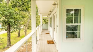 A covered wooden porch with a railing, a light green wall, and a window.
