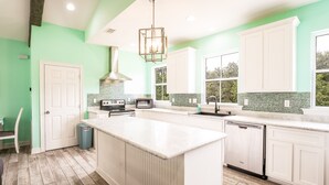 A kitchen with a large island, white cabinets, a green backsplash, and a wooden floor.