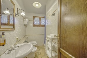 Et badeværelse med vask, toilet og en hylde med håndklæder.