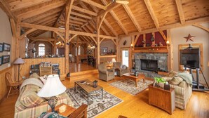A spacious log cabin interior with a high ceiling, a stone fireplace, and a cozy seating area.