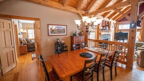 A wooden dining area with a large table and chairs, a chandelier, and a fireplace.