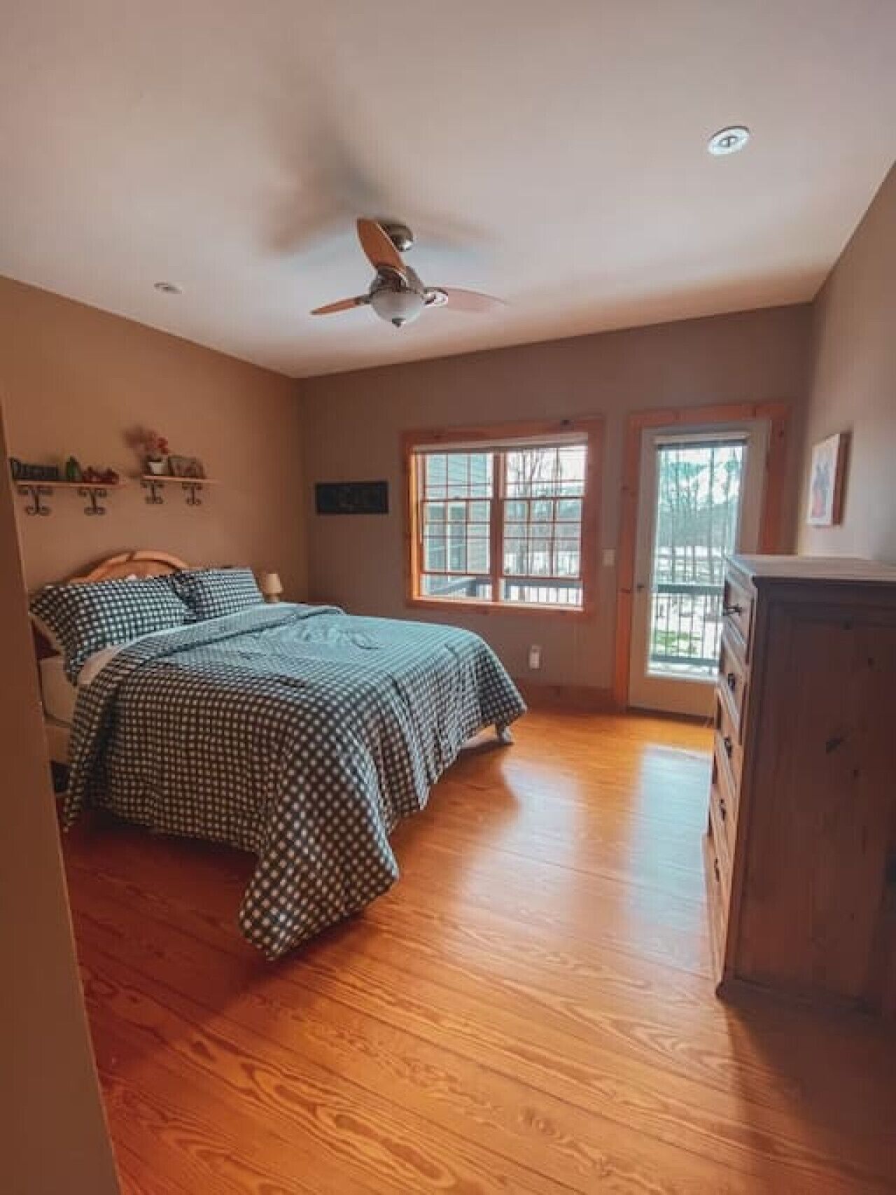 A bedroom with a bed, wooden floor, ceiling fan, window, and a dresser.