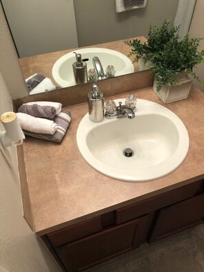 Une salle de bain avec un lavabo blanc, un miroir, une plante en pot et des serviettes.