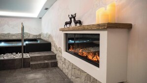A stone fireplace with a glass front, a wooden shelf with deer figurines, and a stone bench. - Apartment "Residence Lastè Catinaccio" with Mountain View, Wi-Fi, Garden & Balcony (Moena)