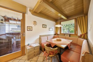 A cozy room with a wooden ceiling, a dining table with a bench, wicker furniture, and a view through a glass door.