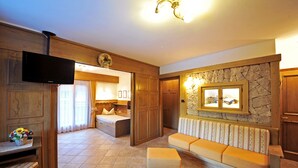 A hotel room with a television, a sofa, a bench, a stone wall, and a wooden door. - Apartment "Residence Lastè Catinaccio" with Mountain View, Wi-Fi, Garden & Balcony (Moena)