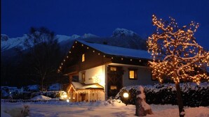 A snow-covered house with string lights and a snow-covered tree. - Apartment "Residence Lastè Catinaccio" with Mountain View, Wi-Fi, Garden & Balcony (Moena)