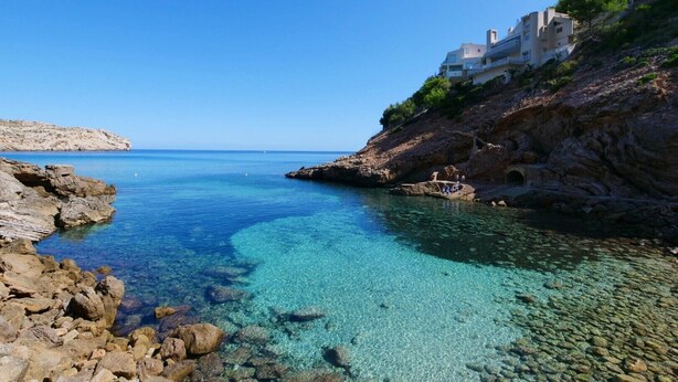 A coastal scene with clear blue water, rocky shore, and a building on a cliff. - Holiday Home 'Can Moragues' with Mountain View, Wi-Fi and Air Conditioning (Pollensa)